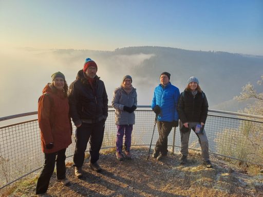 Fünf Personen auf einem Aussichtspunkt, umgeben von Nebel und Bergen.