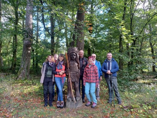 Gruppe von sechs Personen posiert neben einer Holzskulptur eines Löwen im Wald.