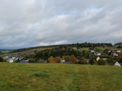 Ländliche Landschaft mit Häusern, Bäumen und bewölktem Himmel.